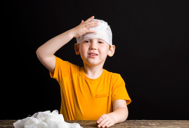 Un beau garçon aux cheveux rouges avec une tête endommagée se bandage avec un bandage médical, un garçon avec du matériel médical pendant l'auto-traitement