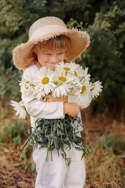 un beau garçon blond dans un chapeau de paille et un costume en lin avec des marguerites dans ses mains