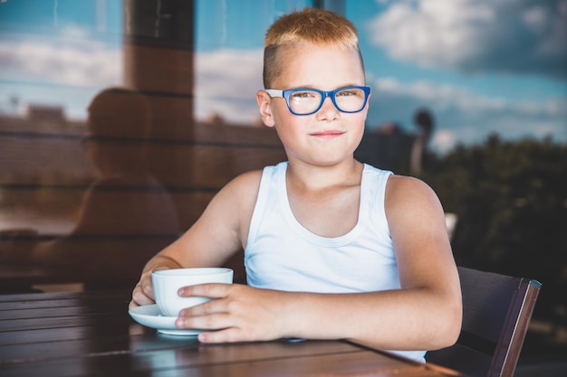 Beau garçon blond dans un t-shirt blanc dans un restaurant buvant du café