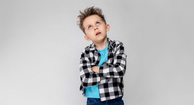 Un beau garçon dans une chemise à carreaux, une chemise bleue et un jean se dresse. Le garçon croisa les bras sur sa poitrine. Le garçon a fermé les yeux