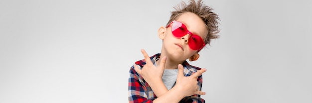 Un beau garçon dans une chemise à carreaux, une chemise grise et un jean se dresse sur gris