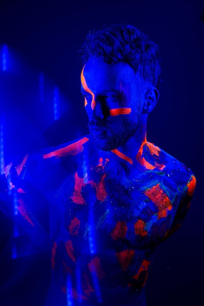 Beau garçon dansant à la rave party avec des peintures fluorescentes sur son visage