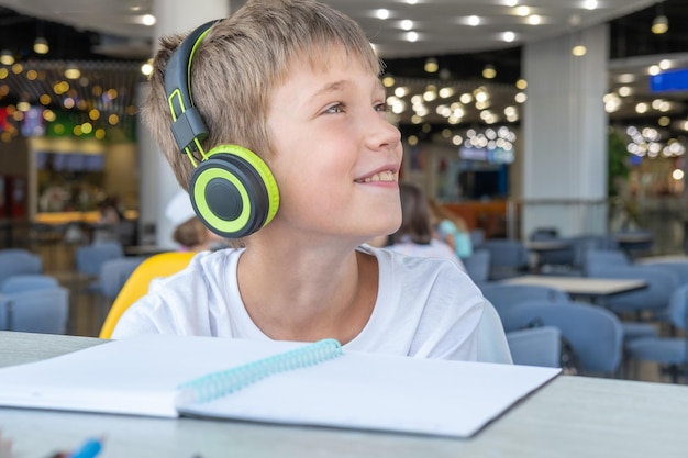 Un beau garçon écoute de la musique avec des écouteurs et écrit ses devoirs dans un cahier dans un café bokeh