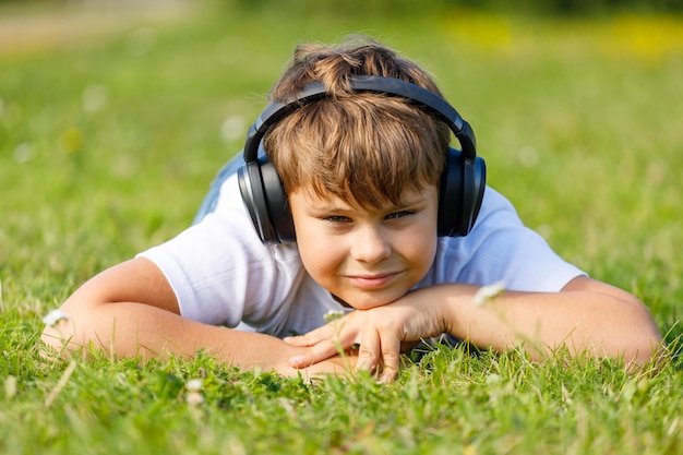 Beau garçon avec des écouteurs écoutant de la musique allongé sur l'herbe