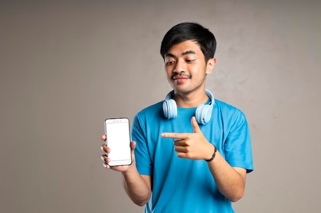 Beau garçon portant un t-shirt bleu et utilisant des écouteurs pointant sur son téléphone portable