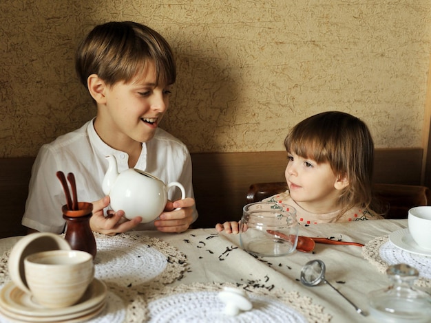 Beau garçon et sa jolie petite soeur sont assis à la table de la cuisine à la maison et font du thé
