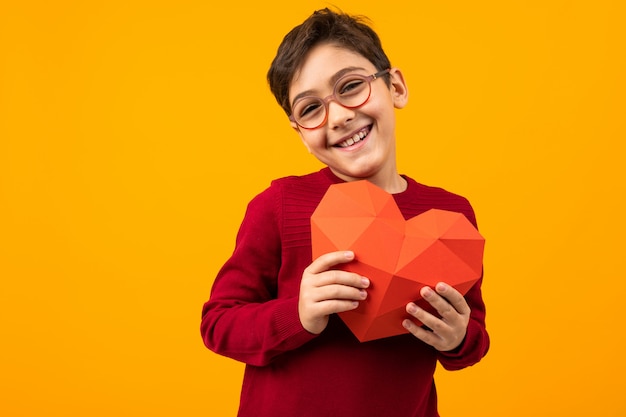 Beau garçon souriant avec coeur de papier pour la Saint Valentin sur fond jaune