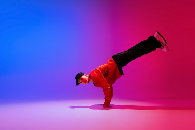 Beau garçon sportif dansant le hip-hop dans des vêtements élégants sur un mur dégradé coloré à la salle de danse à la lumière du néon. Culture jeunesse, mouvement, style et mode, action. Portrait lumineux à la mode.