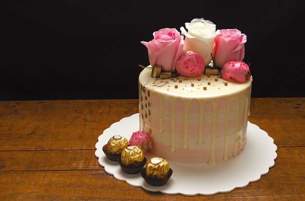 Beau gâteau décoré de roses naturelles et de chocolats sur table en bois