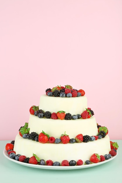 Beau gâteau de mariage avec des baies sur fond rose