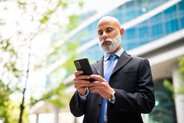 Un beau gestionnaire chauve à l'époque qui utilise un smartphone en plein air.