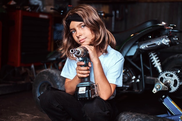 Un beau gosse pensif pose avec un tournevis à l'atelier de service automobile.