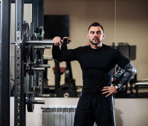 Beau avec gros muscles posant à côté de la barre