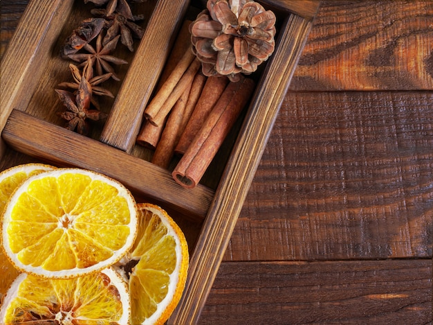 Beau gros plan d'oranges sèches, de bâtons de cannelle et d'Anis étoilé, cônes de sapin dans une boîte en bois