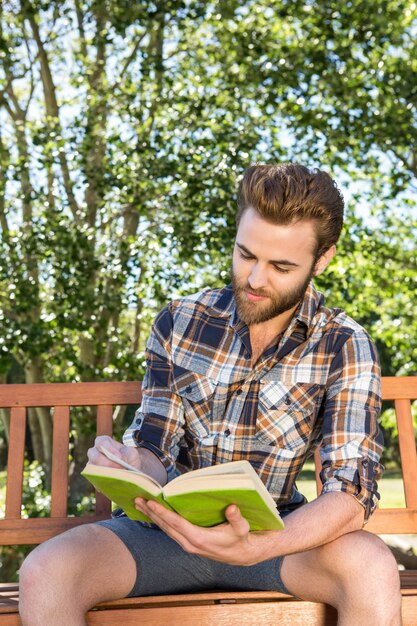 Beau hipster lisant dans le parc