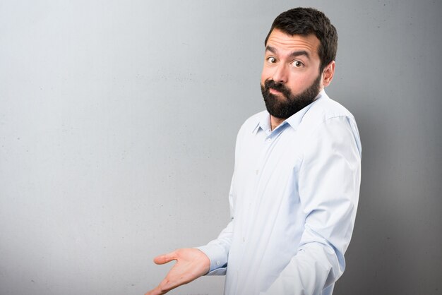 Beau homme à la barbe faisant un geste sans importance sur un fond texturé