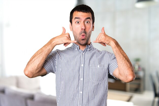 Beau homme faisant un geste téléphonique à l&#39;intérieur de la maison