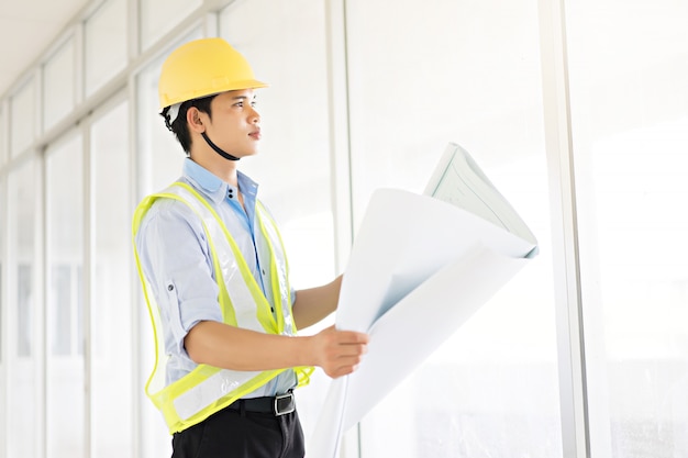 Beau ingénieur tenant blueprint et souriant au bureau.