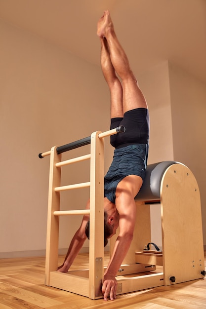 Beau instructeur masculin de pilates effectuant des exercices de remise en forme d'équilibre d'étirement sur un petit équipement de baril au studio de pilates intérieur intérieur moderne