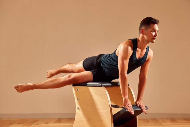 Un beau instructeur de pilates effectuant un exercice de fitness d'équilibre d'étirement sur un petit baril