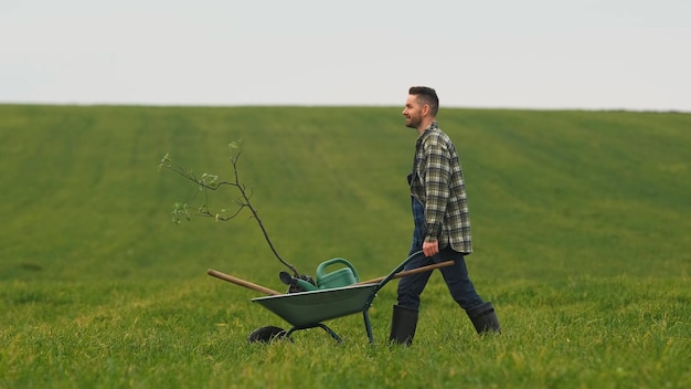 Le beau jardinier marchant avec une brouette à travers le champ