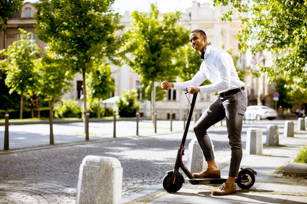 Beau jeune afro-américain à l'aide d'un scooter électrique dans la rue