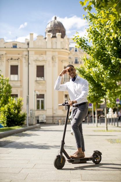 Beau jeune afro-américain utilisant un scooter électrique dans une rue