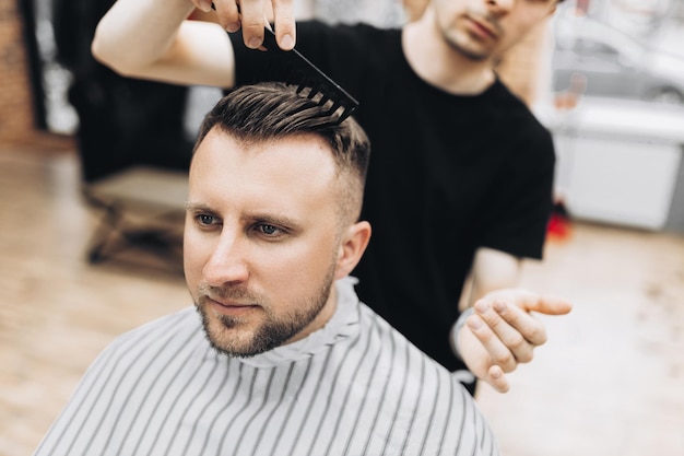 beau jeune barbu assis dans un fauteuil dans un salon de beauté et le coiffeur près de lui