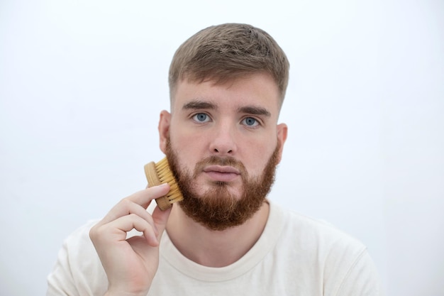 Beau jeune barbu homme brutal européen avec un poil de barbe se peigne la barbe sur le visage avec un