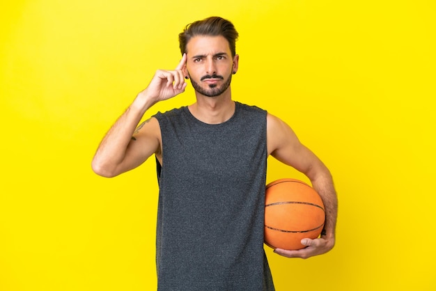 Beau jeune basketteur homme isolé sur fond jaune ayant des doutes et pensant