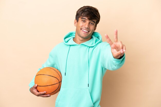 Beau jeune basketteur homme isolé sur fond ocre souriant et montrant le signe de la victoire