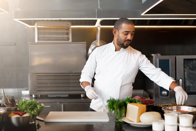 Photo beau jeune chef africain debout dans une cuisine professionnelle dans un restaurant en train de préparer un repas de viande