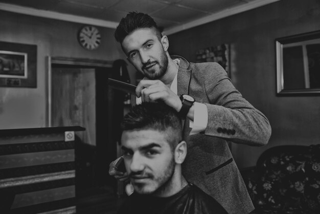 Beau jeune coiffeur donnant une nouvelle coupe de cheveux au client masculin au salon