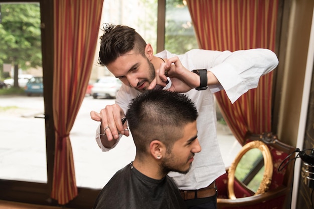 Beau jeune coiffeur donnant une nouvelle coupe de cheveux au client masculin au salon