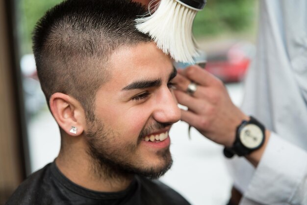 Beau jeune coiffeur donnant une nouvelle coupe de cheveux au client masculin au salon