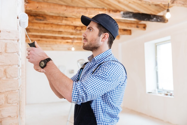 Beau jeune constructeur travaillant avec un rouleau à peinture à l'intérieur