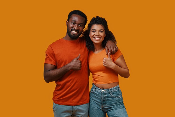 Beau jeune couple africain gesticulant et souriant en se tenant debout sur fond jaune