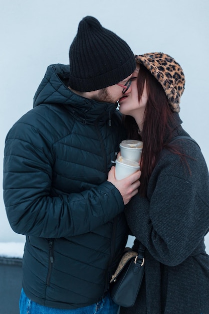 Un beau jeune couple d'amants en vêtements d'hiver élégants buvant du café et s'embrassant relations d'amour et sentiments