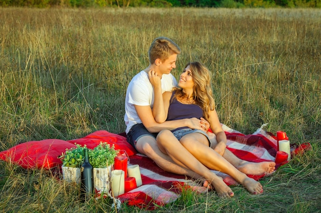 Beau jeune couple d'amoureux heureux en pique-nique allongé sur un plaid le jour d'été ensoleillé, profitant et se reposant. étreignant et se regardant et souriant.