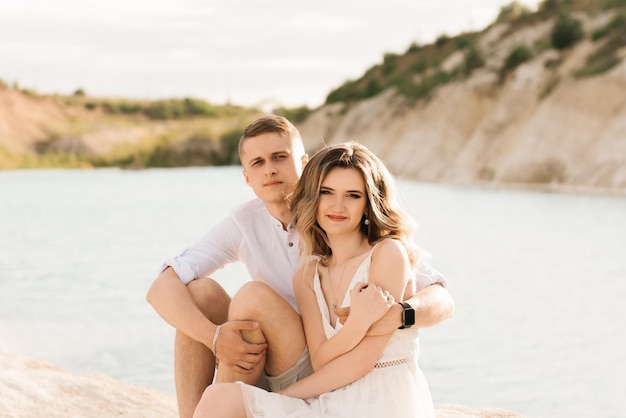 Un beau jeune couple amoureux un homme et une femme s'embrassent près d'un lac bleu et du sable au coucher du soleil Vacances à la mer sur la plage coucher de soleil matin lune de miel tropiques océan fille relation