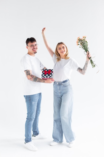 Beau jeune couple amoureux à la maison célébrant avec une boîte-cadeau et des fleurs