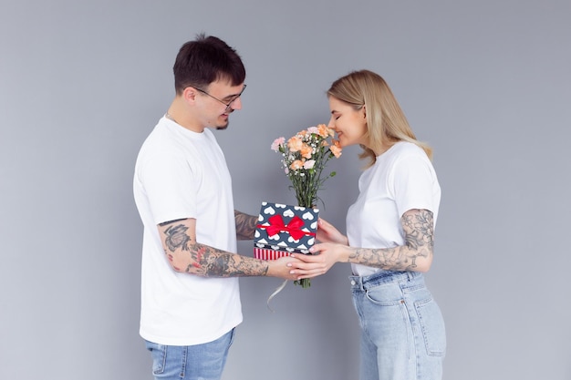 Beau jeune couple amoureux à la maison célébrant avec une boîte-cadeau et des fleurs