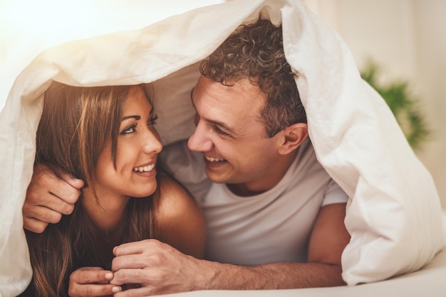 Un beau jeune couple d'amoureux se regarde avec amour et passe une matinée paresseuse au lit recouvert d'une couverture.