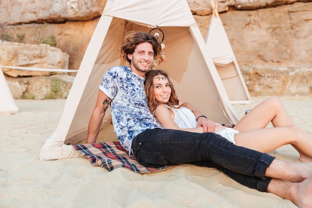 Beau jeune couple assis dans un tipi sur la plage