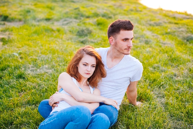 Le beau jeune couple assis sur l'herbe et rêvant en regardant de côté