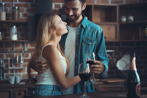 Beau jeune couple boit du vin et sourit en cuisinant dans la cuisine à la maison