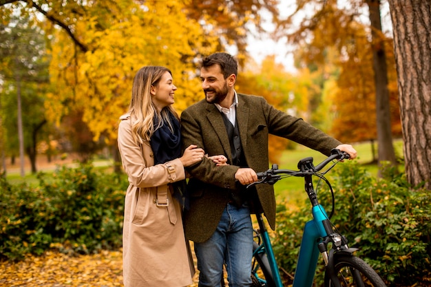 Beau jeune couple dans le parc en automne avec vélo électrique