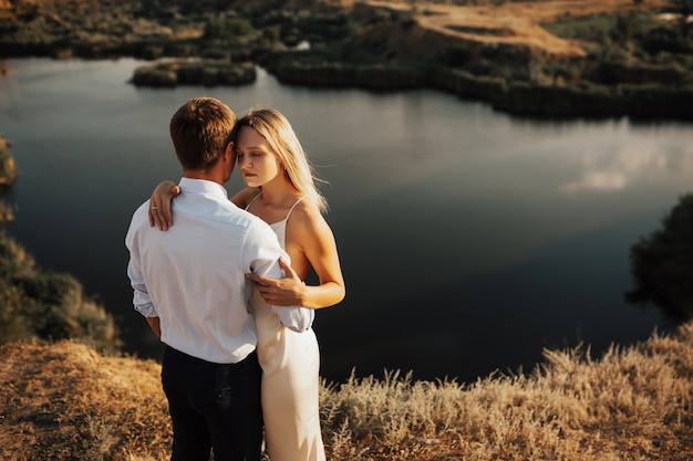 Beau jeune couple dans des vêtements élégants serrant près du lac au sommet de la colline.