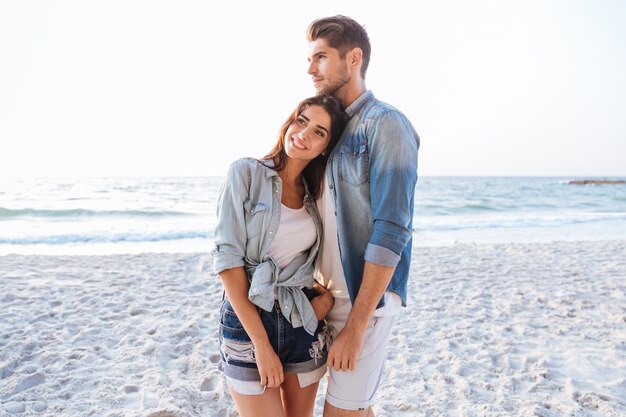 Beau jeune couple debout et rêvant sur la plage ensemble