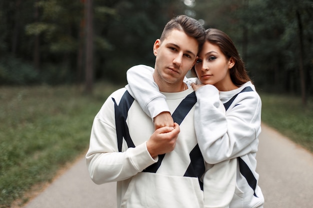 Beau jeune couple élégant en chandails blancs identiques serrant dans les bois